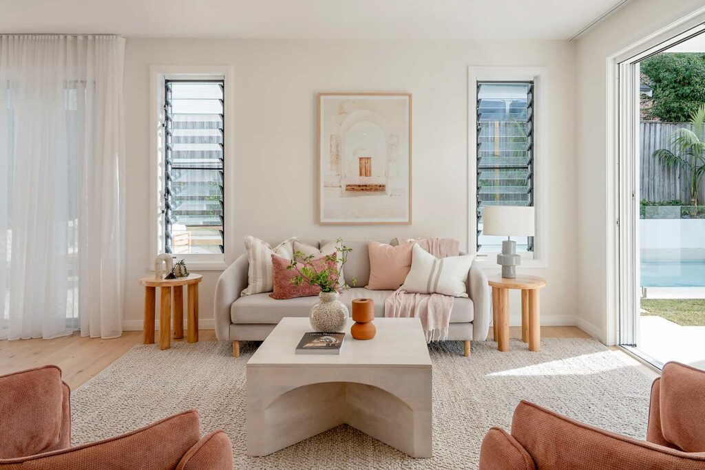 Warm Hamptons inspired lounge room design with pink, earthy furnishings and view out to alfresco and pool